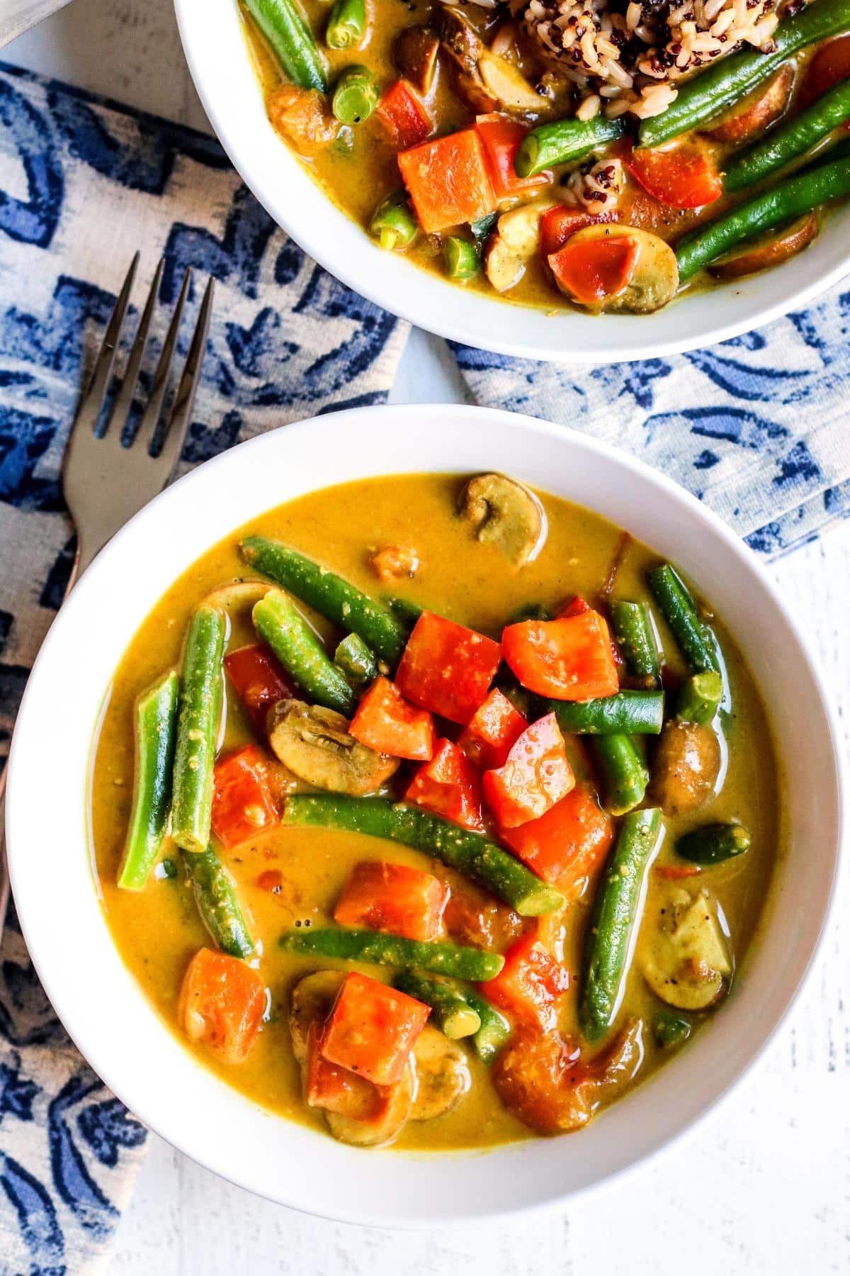 Bowls of green bean curry and a blue and white napkin.