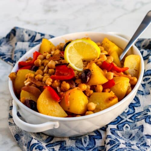 Casserole dish filled with roasted potatoes and chickpeas and garnished with lemon.