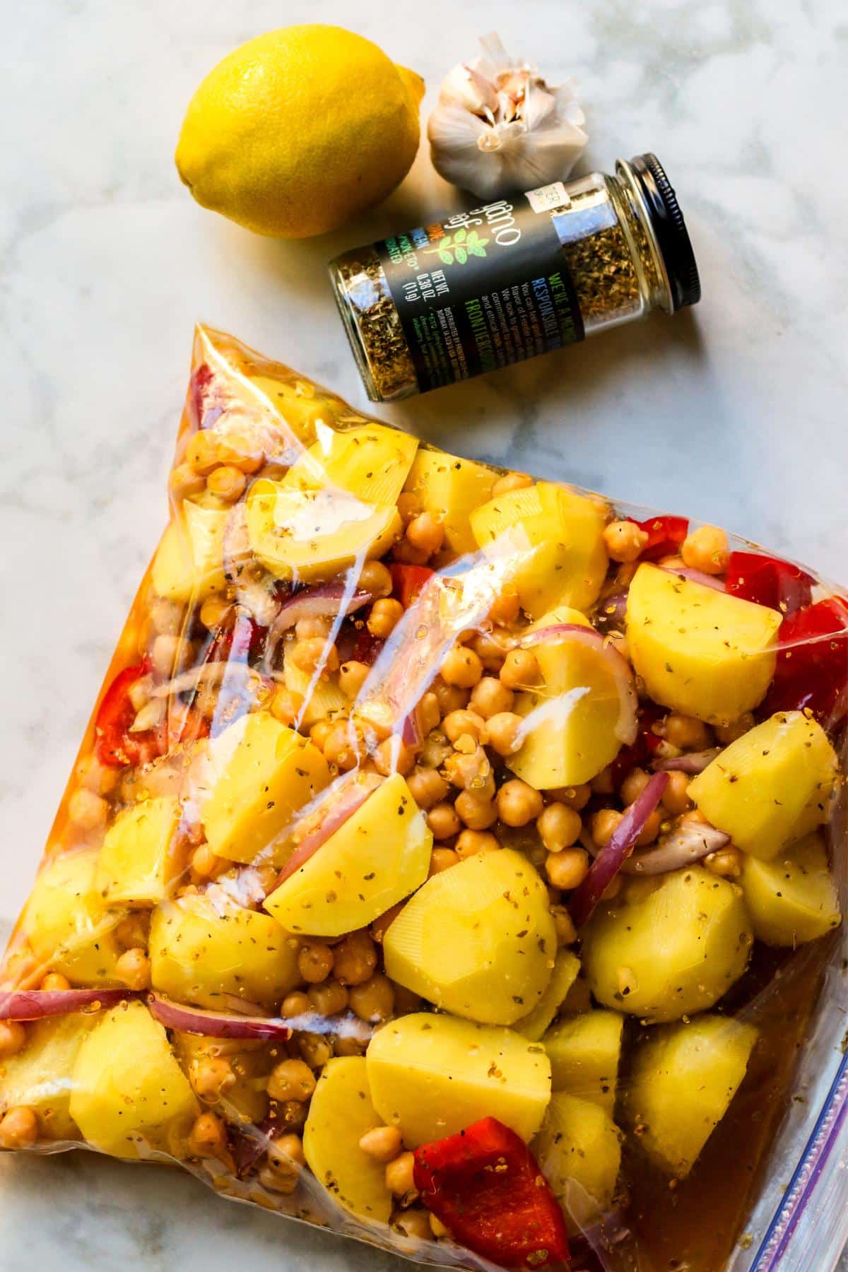 Lemon, garlic, and jar of oregano next to a large bag filled with the ingredients marinating.