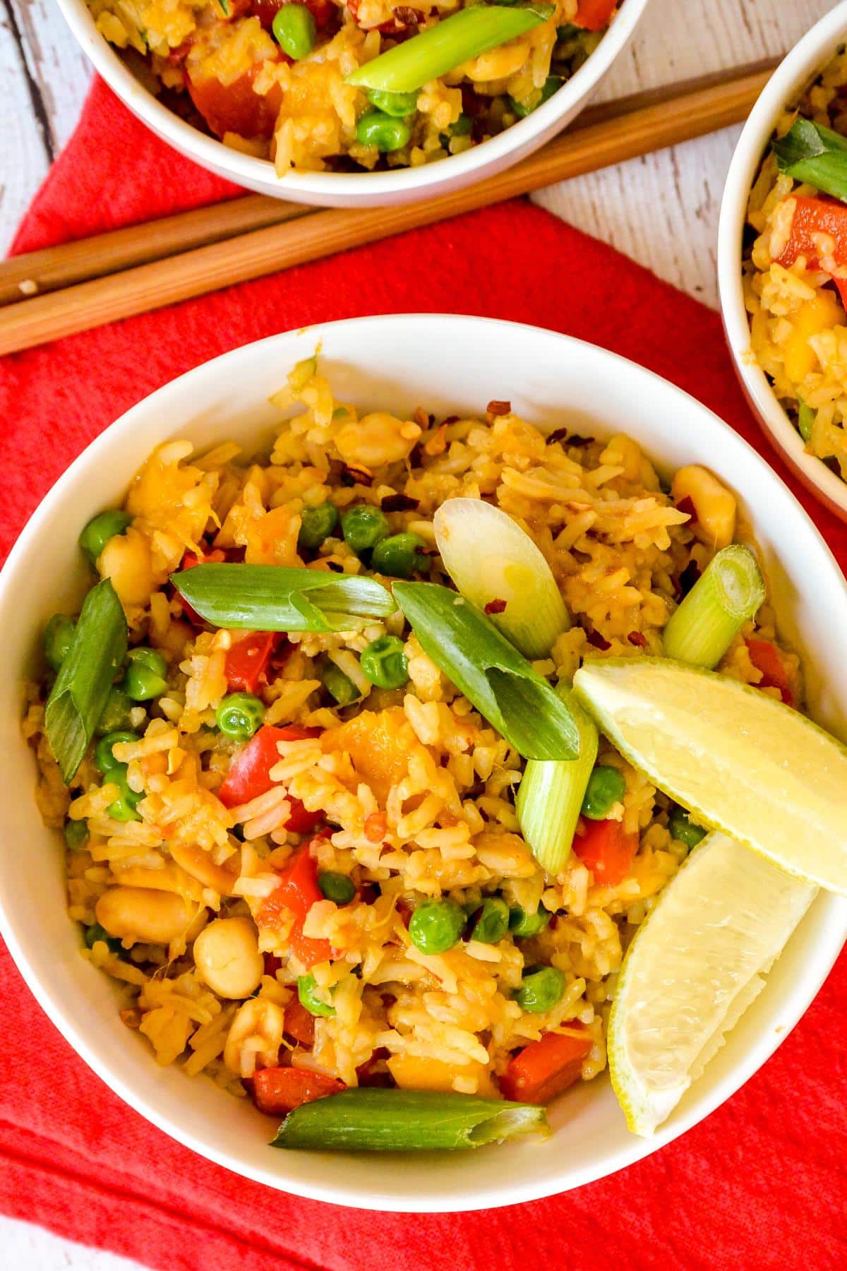 Mango fried rice in a large bowl garnished with green onions and lime wedges.