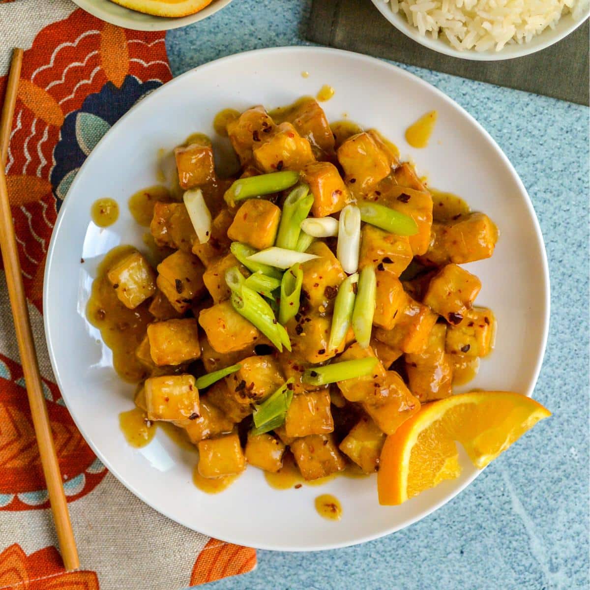Platter of crispy tofu cubes tossed in orange sauce and garnished with green onions.