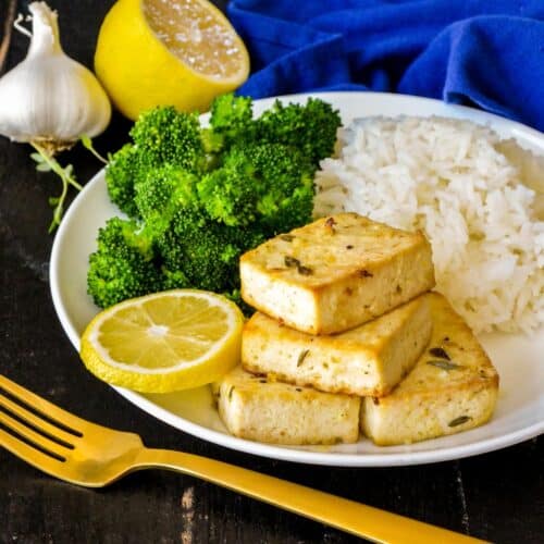 Baked tofu steaks on a plate with rice, broccoli, and a slice of lemon.