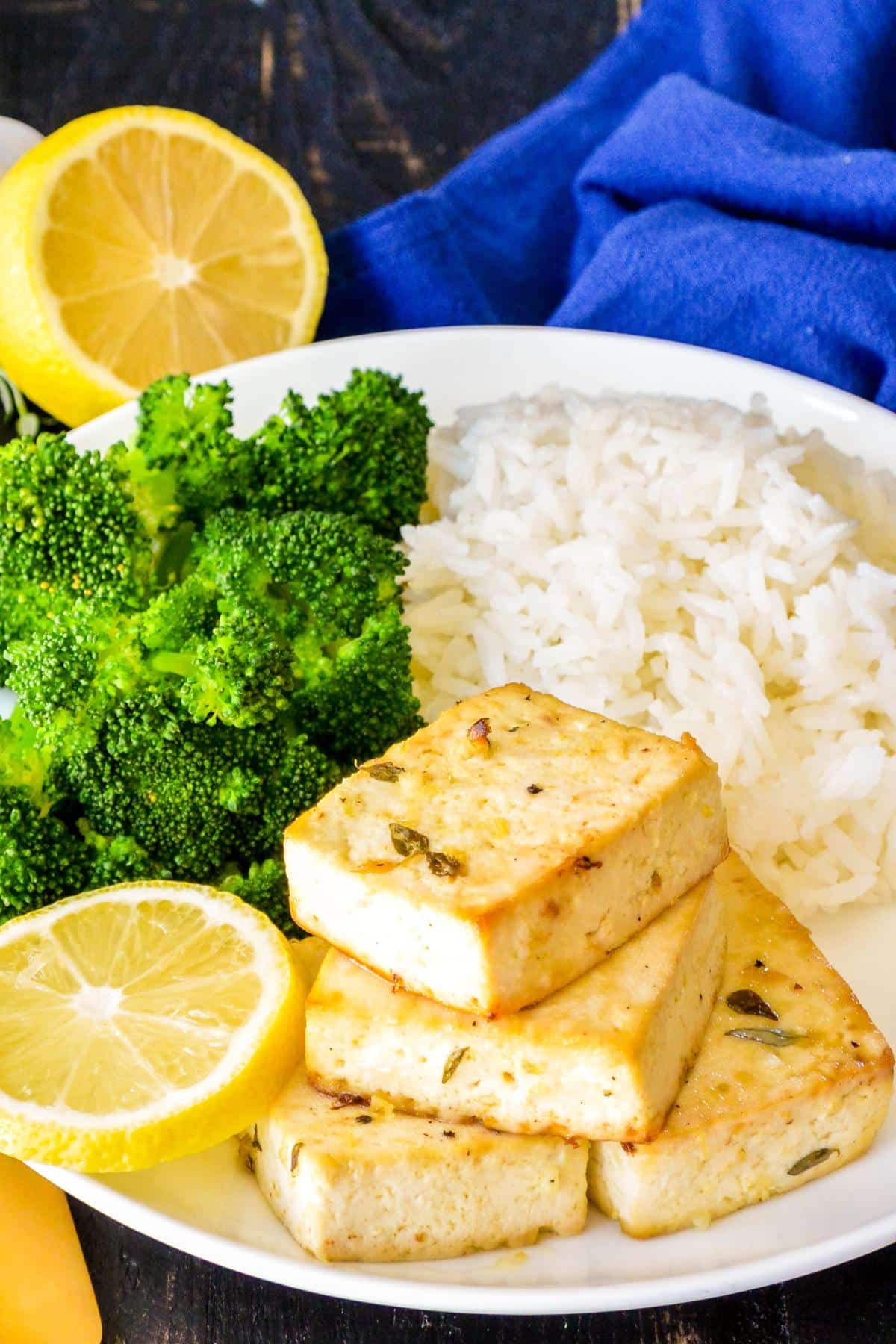 Tofu on a dinner plate with a lemon slice, streamed broccoli, and rice.