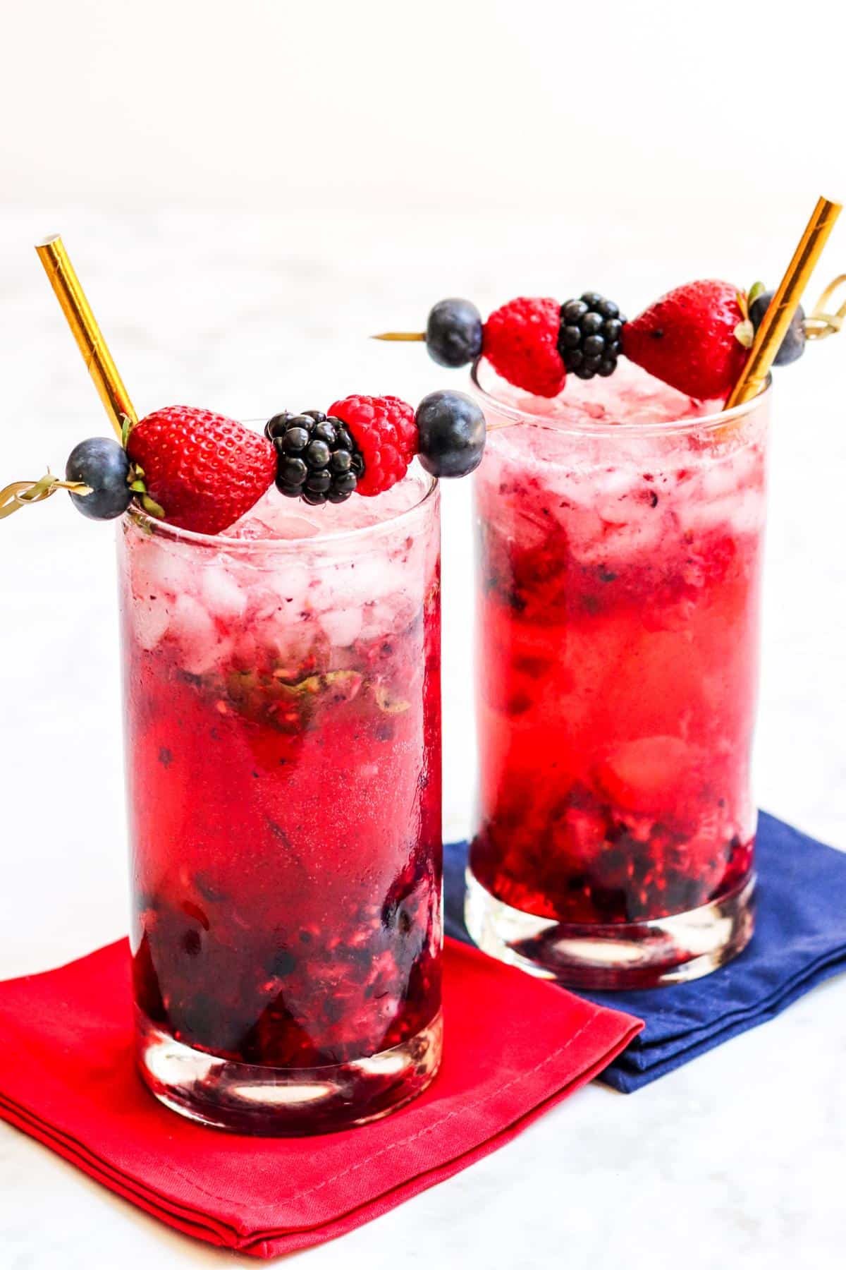 Two cocktails with gold straws and fresh berry garnishes.