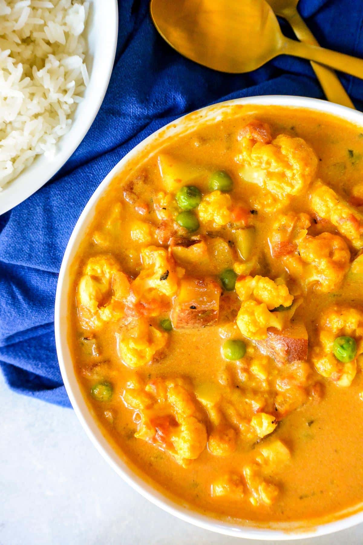 Pot of cauliflower coconut curry and bowl of rice with gold serving spoons.