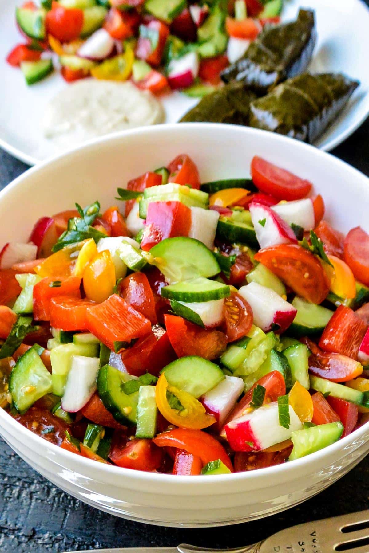 Bowl of salad and a plate with salad, hummus, and stuffed grape leaves.