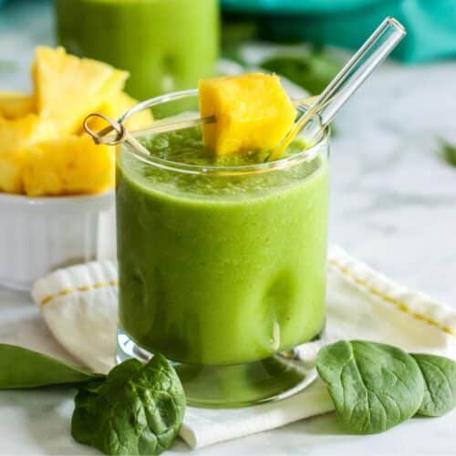 Green smoothie in a glass garnished with a chunk of fresh pineapple.