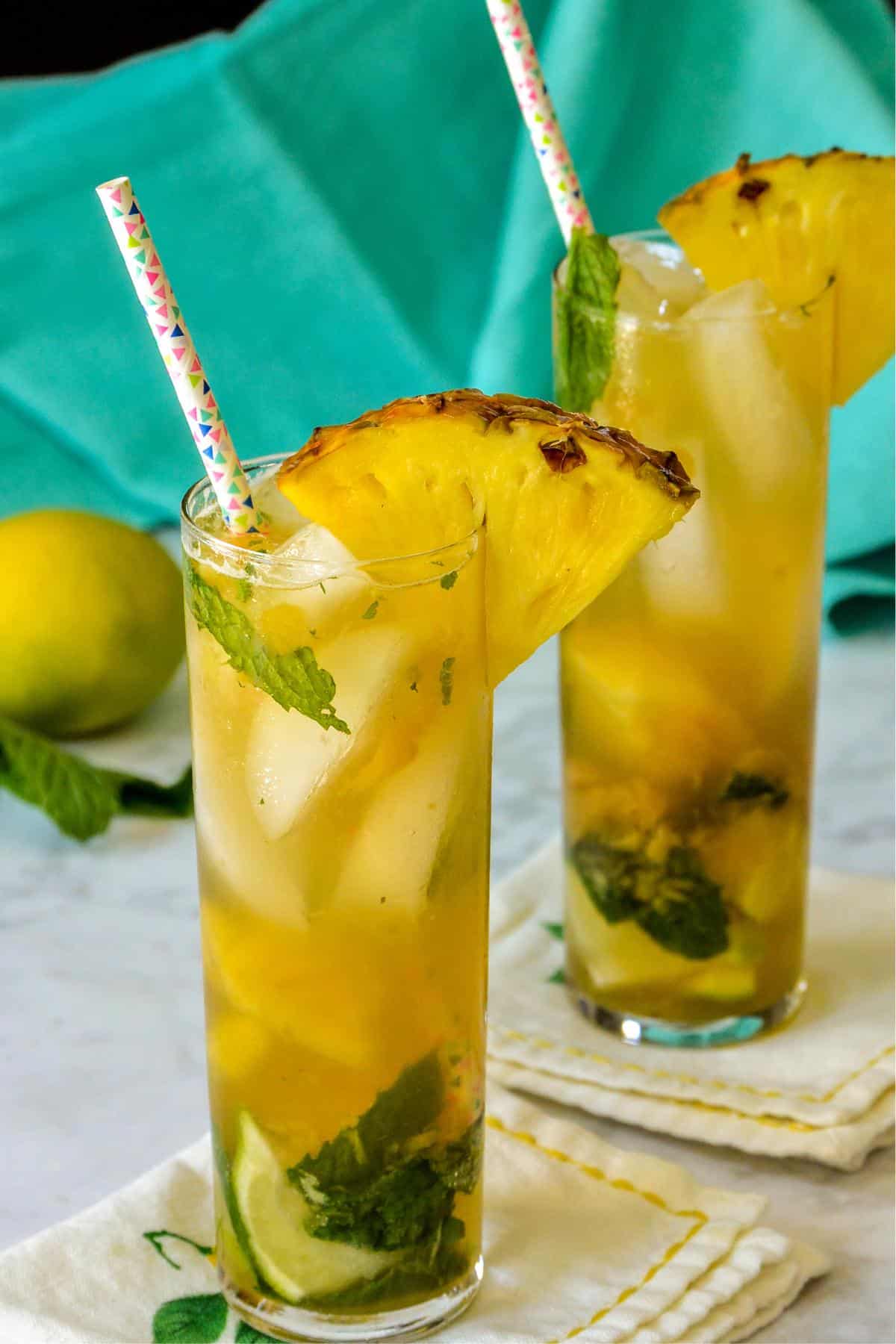 Tall glasses of pineapple mojitos with straws and pineapple wedge garnishes.