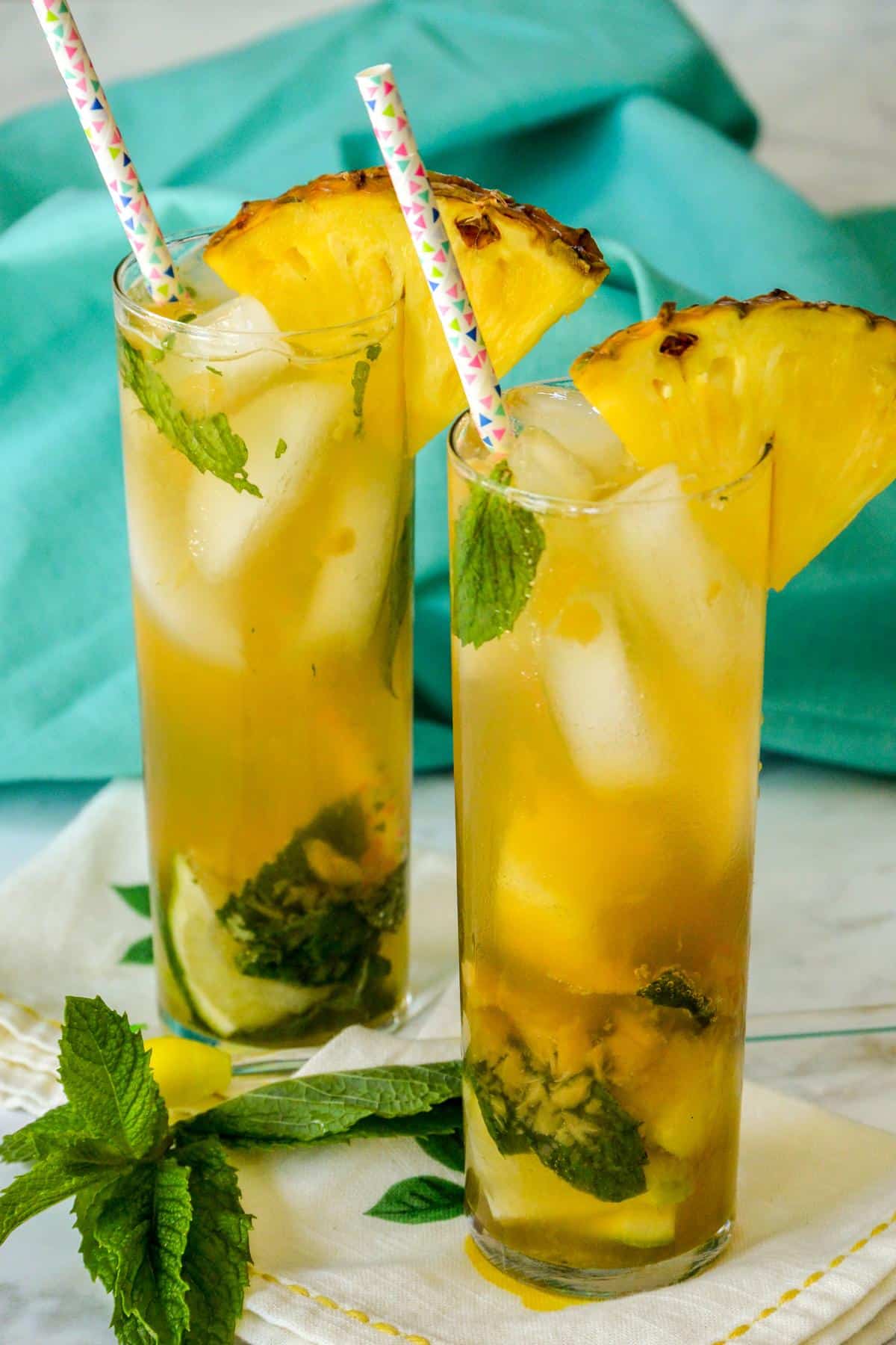 Two cocktails with pineapple wedges and fresh mint leaves.