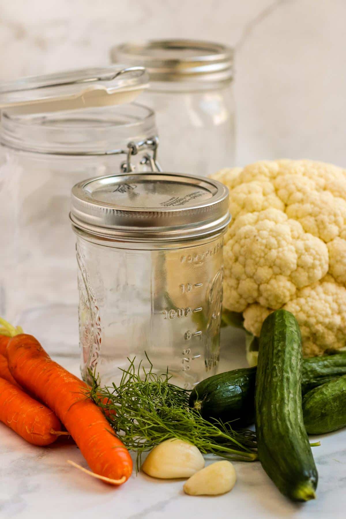 Carrots, cucumbers, cauliflower, garlic cloves, fresh dill, and empty jars.