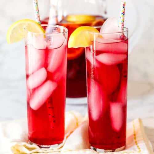 Glasses and pitcher of spiked iced tea with lemon wedges.