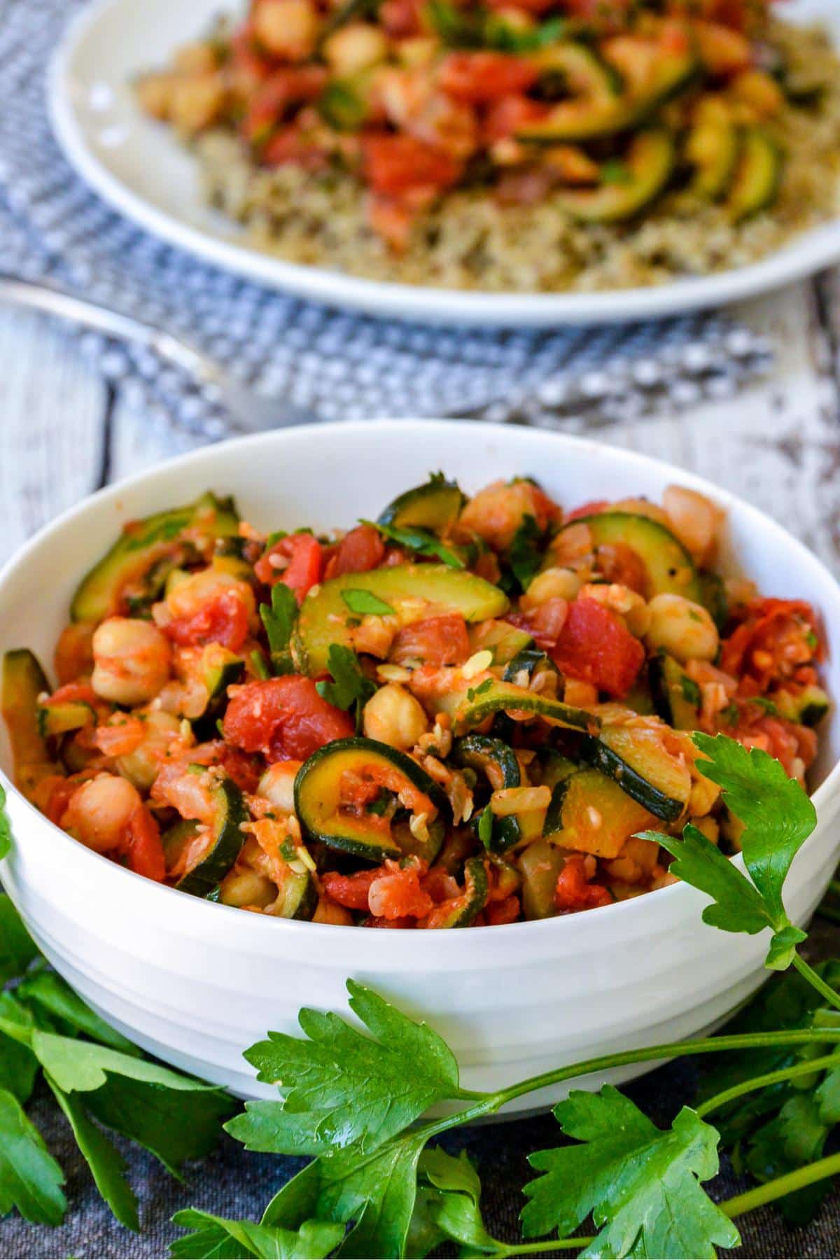 Bowl of stewed zucchini and a plate of quinoa topped with the vegetables.