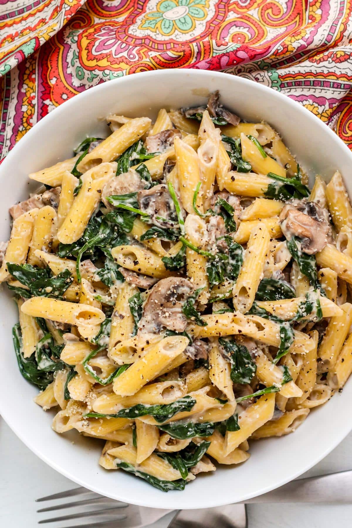 Bowl of vegan spinach mushroom pasta with a paisley napkin.