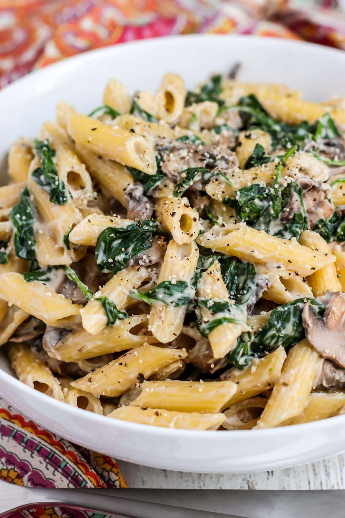 Bowl of penne in a creamy sauce with spinach and mushrooms.