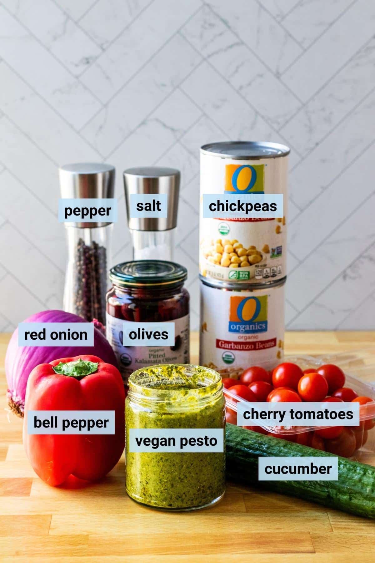 Ingredients needed to make this recipe: cans of chickpeas, cherry tomatoes, cucumber, vegan pesto sauce, red bell pepper, red onion, Kalamata olives, and salt and pepper.