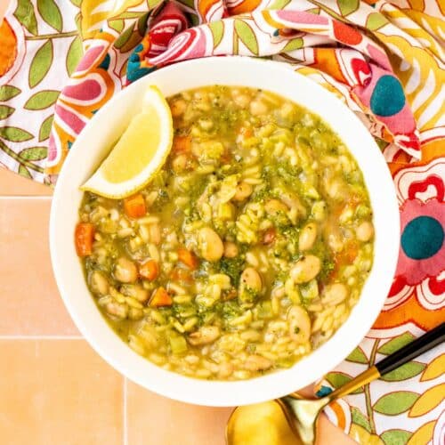 Bowl of Vegan Pesto Orzo Soup garnished with a lemon wedge.