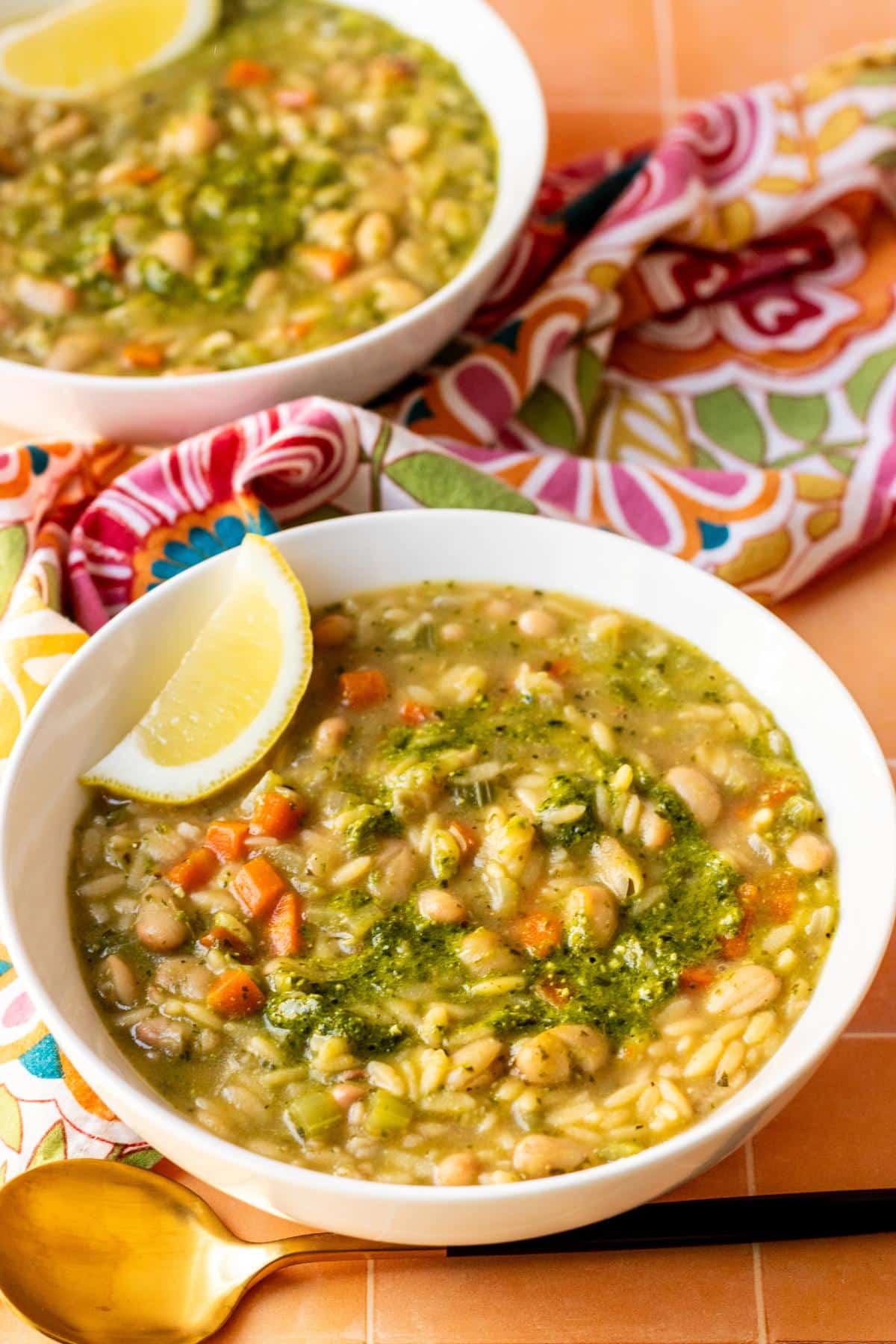 Bowls of Vegan Pesto Orzo Soup garnished with lemon wedges.