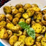 Roasted pesto potatoes in a serving bowl garnished with a sprig of fresh basil.