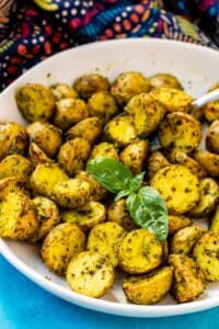 Roasted pesto potatoes in a serving bowl garnished with a sprig of fresh basil.