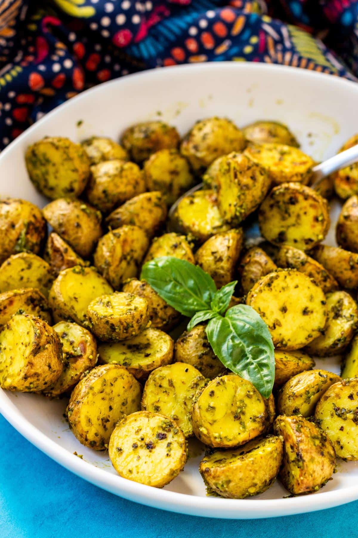Roasted pesto potatoes in a serving bowl garnished with a sprig of fresh basil.