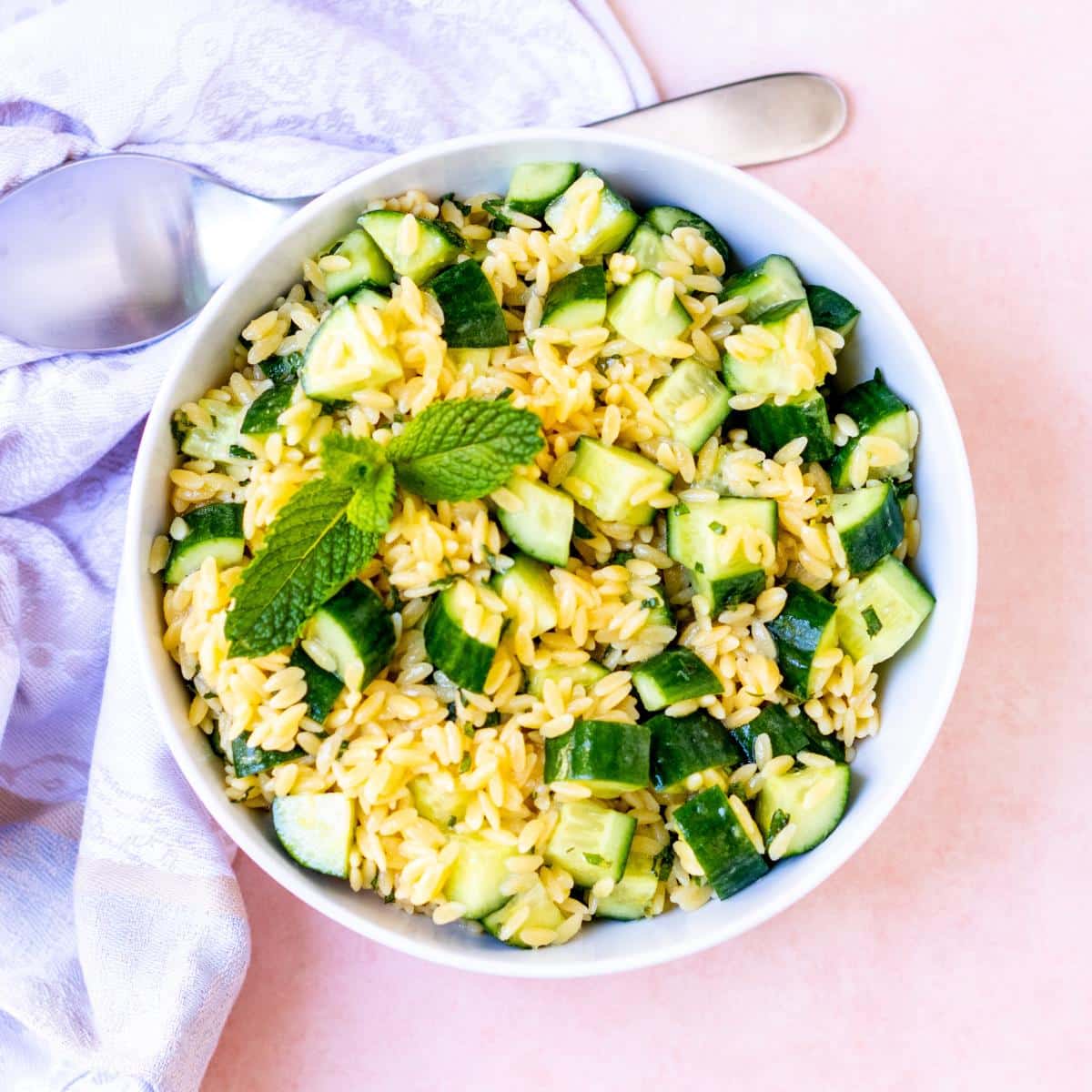 Bowl of lemon cucumber orzo salad garnished with a sprig of fresh mint.