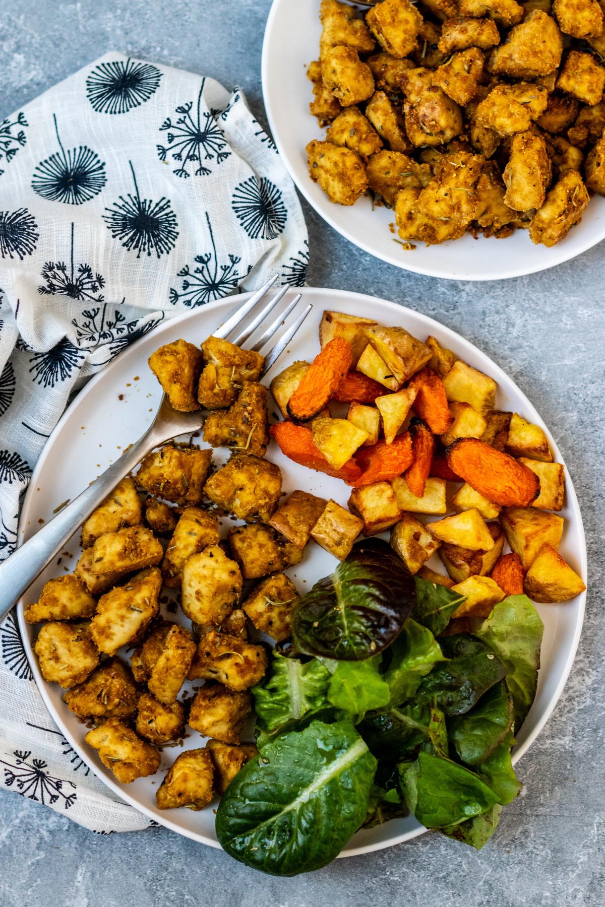 Plate of rosemary tofu and dinner plate with tofu, roasted potatoes and carrots, and a green salad.