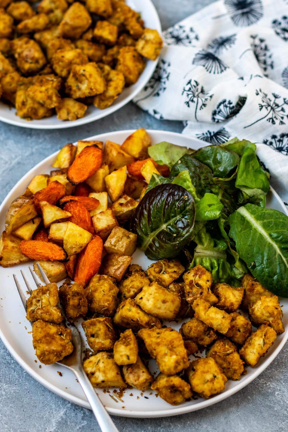 Rosemary tofu on a dinner plate with roasted potatoes and carrots and a green salad.