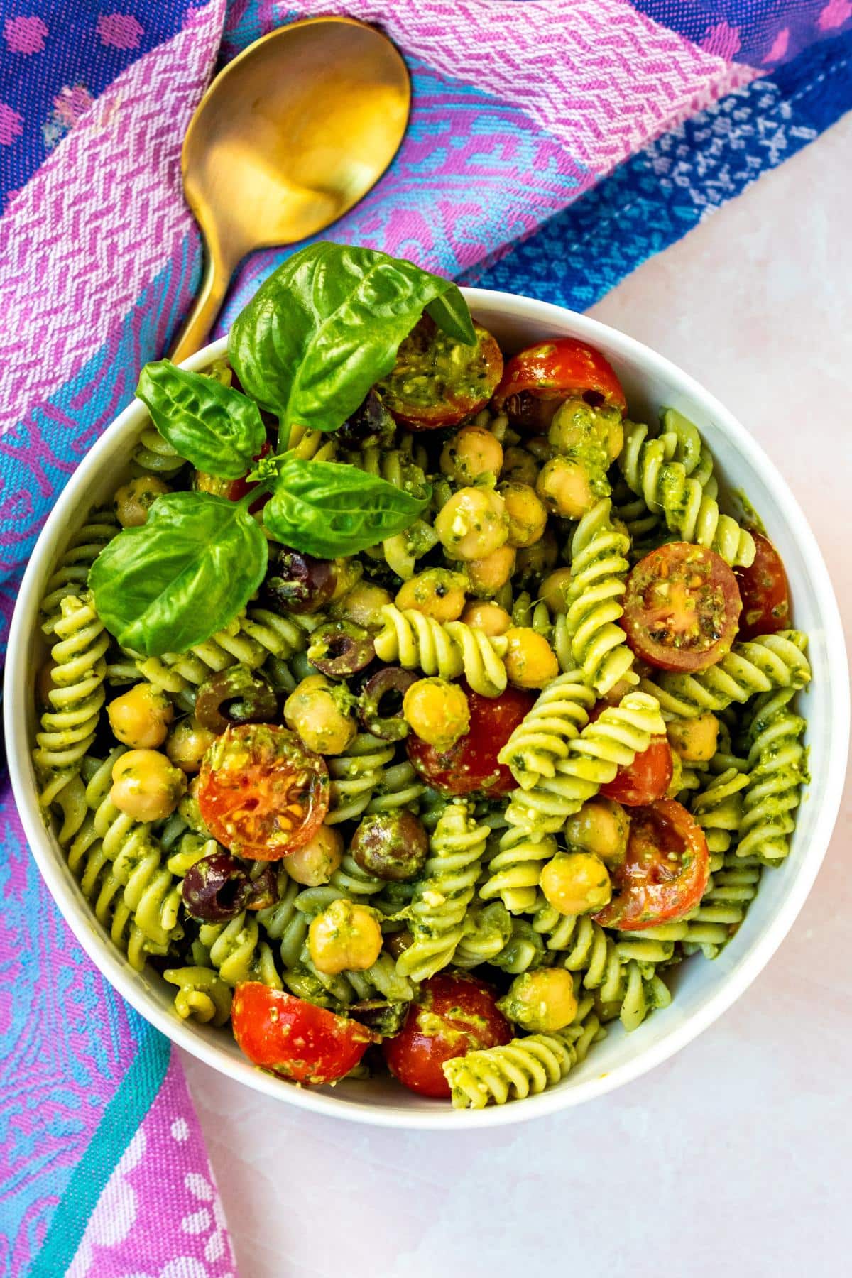 Bowl of pasta salad made with corkscrew noodles, cherry tomatoes, chickpeas, olives, and pesto sauce.