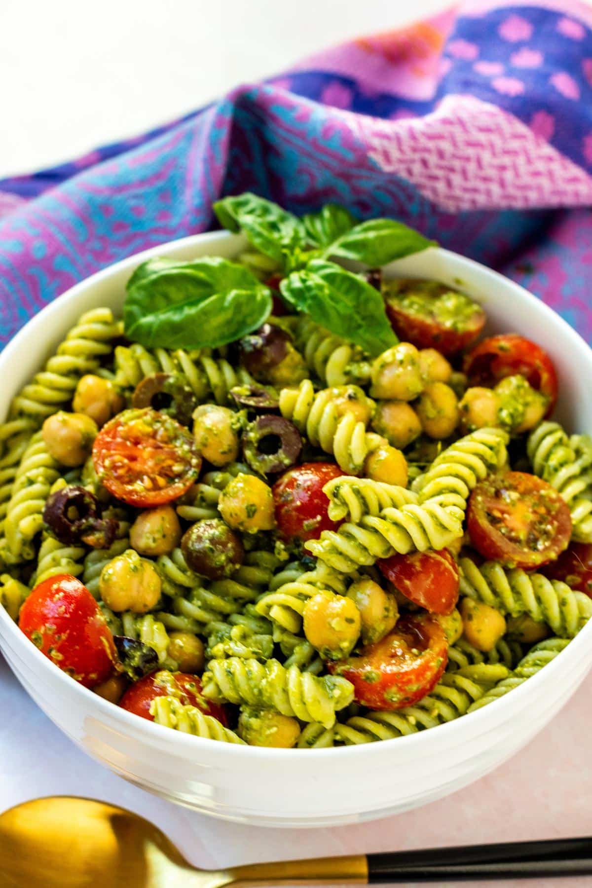 Serving bowl of pesto pasta salad with a gold spoon.