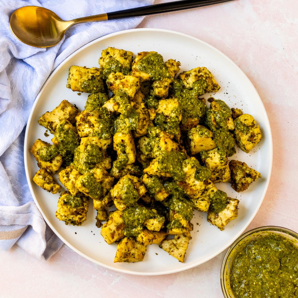 Baked tofu chunks on a plate drizzled with pesto sauce.