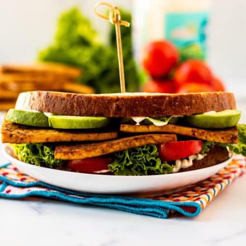 Sandwich on a plate made with avocado, tofu, tomato, and lettuce on sourdough bread.