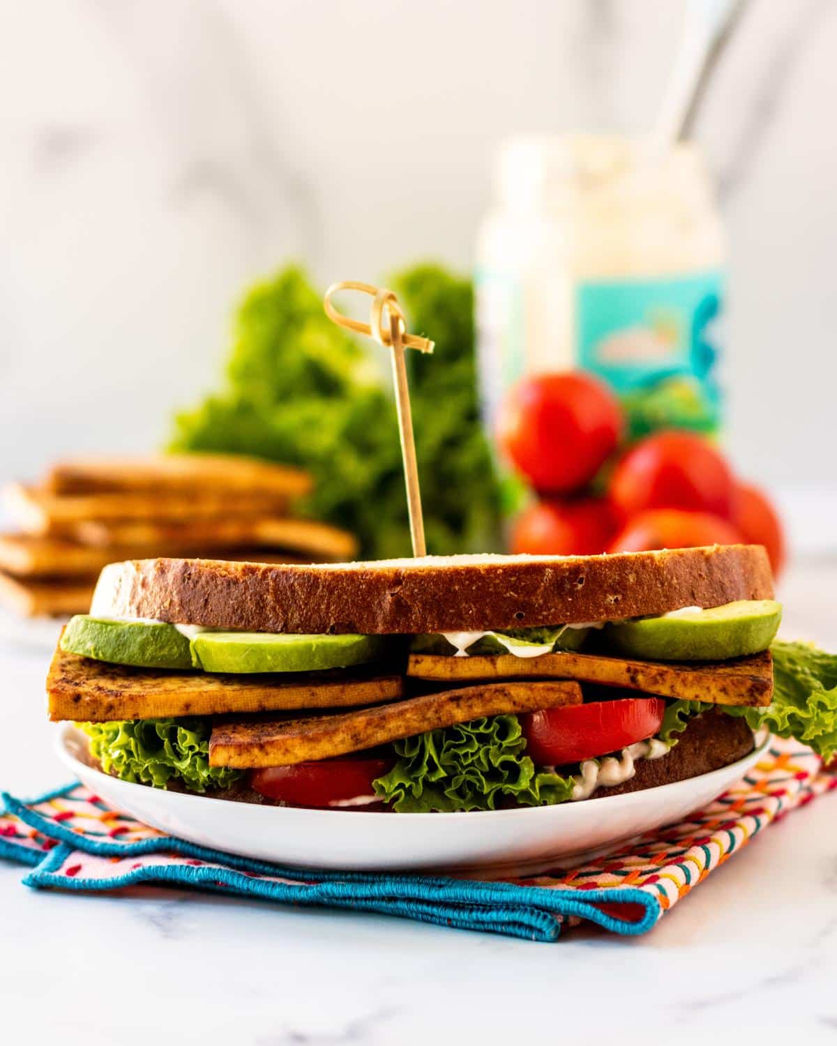 Sandwich made with baked tofu, avocado, tomatoes, lettuce, and sourdough bread.