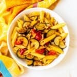 Bowl of penne with tomatoes, zucchini, and pine nuts.