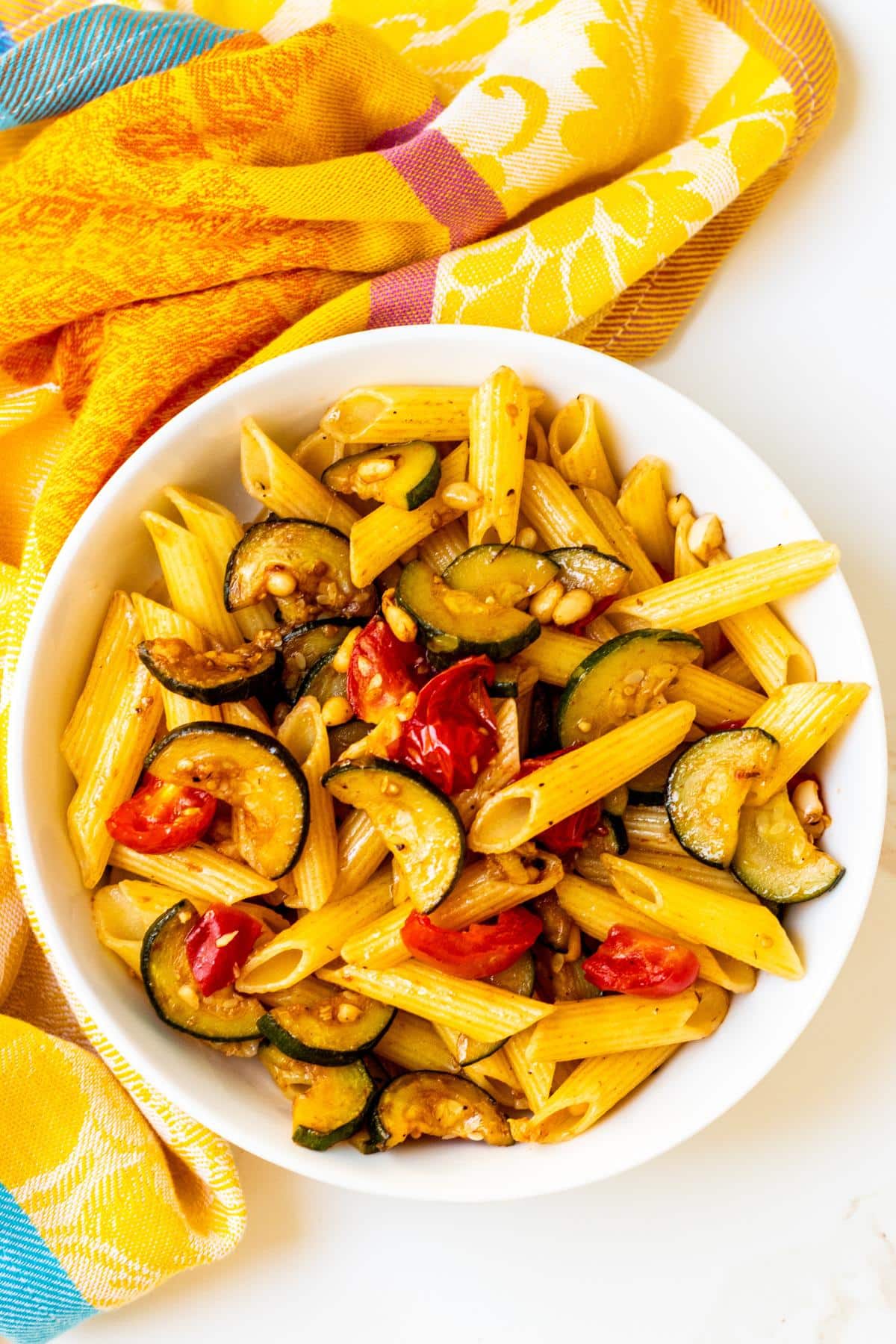 Bowl of penne pasta with tomatoes, zucchini, and pine nuts.