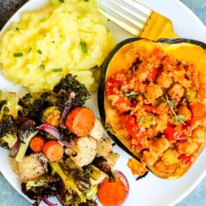 Roasted vegetables, olive oil mashed potatoes, and chickpea quinoa stuffed acorn squash on a plate with a gold fork.