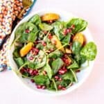 Bowl of spinach salad with oranges, pomegranate arils, and pumpkin seeds.