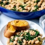 Serving of beans and spinach on a plate with slices of toasted baguette.