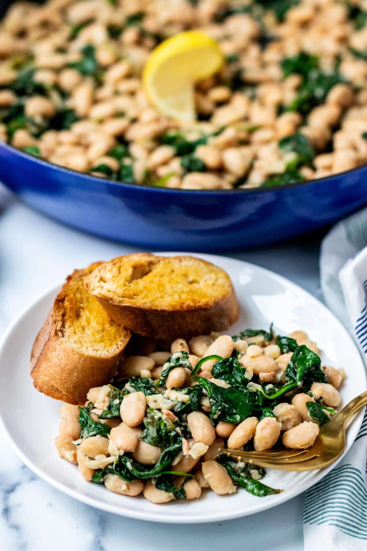 Serving of beans and spinach on a plate with slices of toasted baguette.