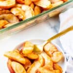 A serving of baked apples on a small plate with a gold spoon.