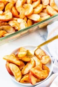 A serving of baked apples on a small plate with a gold spoon.
