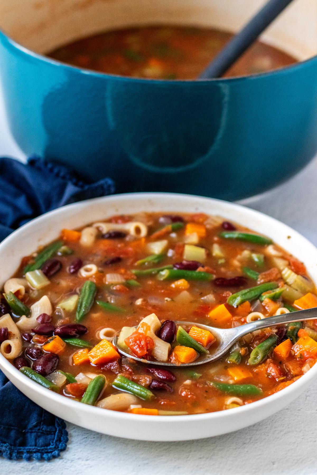 Pot of soup and bowl of minestrone with a spoon in it.