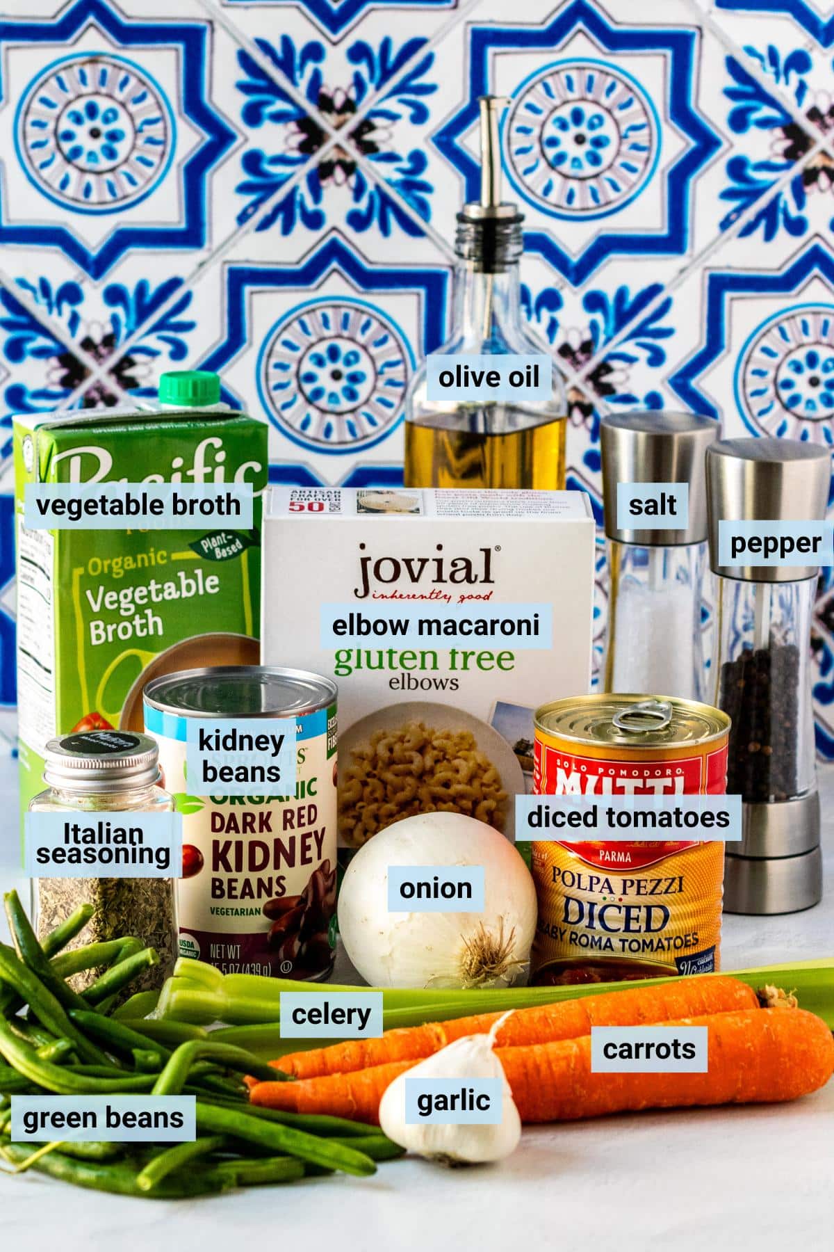 Fresh green beans, garlic, celery, carrots, onion, can of kidney beans, can of diced tomatoes, carton of vegetable broth, box of elbow noodles, bottle of olive oil, and salt and pepper grinders.