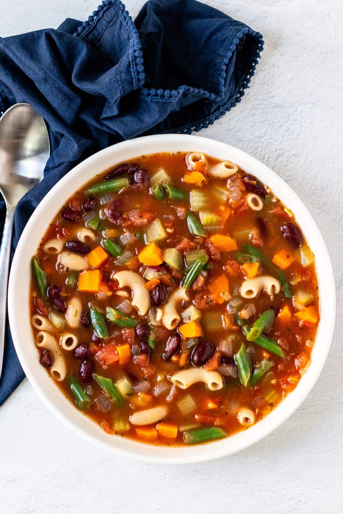 Bowl of minestrone soup with a spoon and blue napkin.