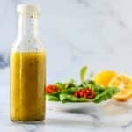 Bottle of dressing, a green salad, and a lemon.