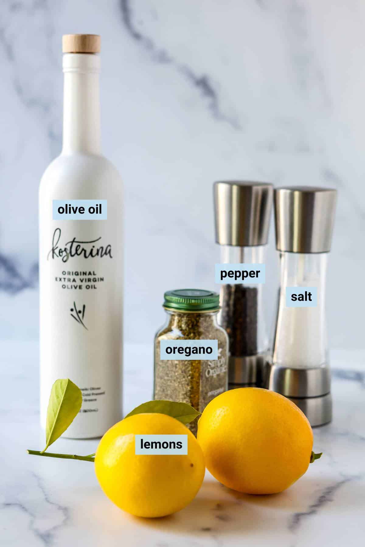 Lemons, bottle of olive oil, jar of dried oregano, and salt and pepper grinders.