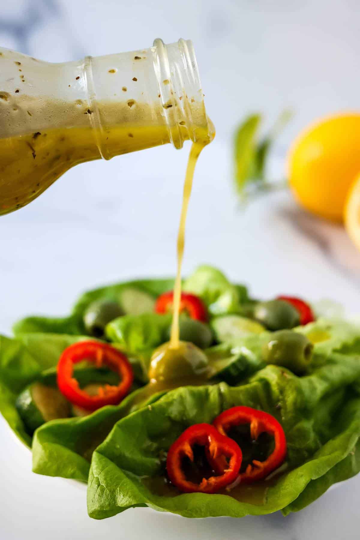 Lemon Olive Oil Dressing being poured over a salad with butter lettuce, red bell peppers, and green olives.