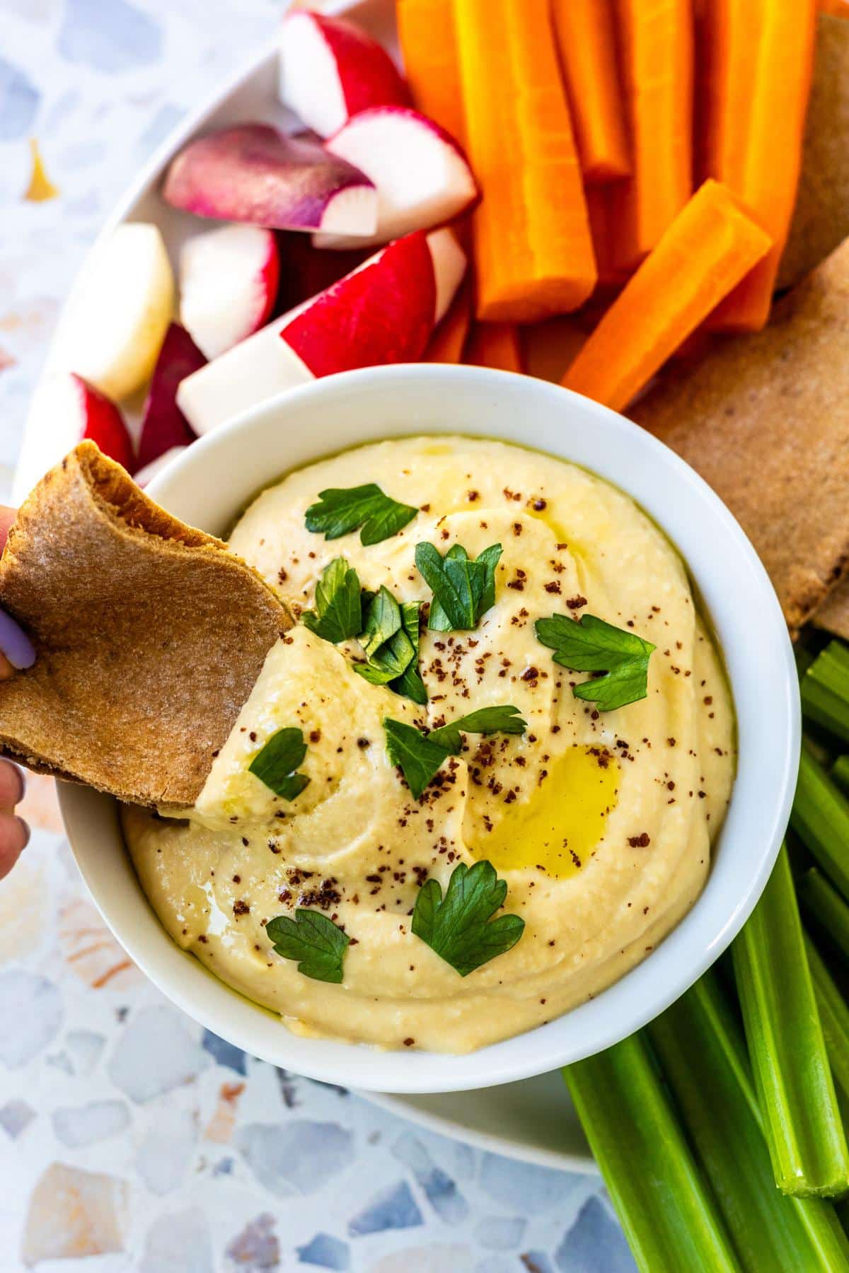 Hand dipping a triangle of pita bread into a bowl of dip.