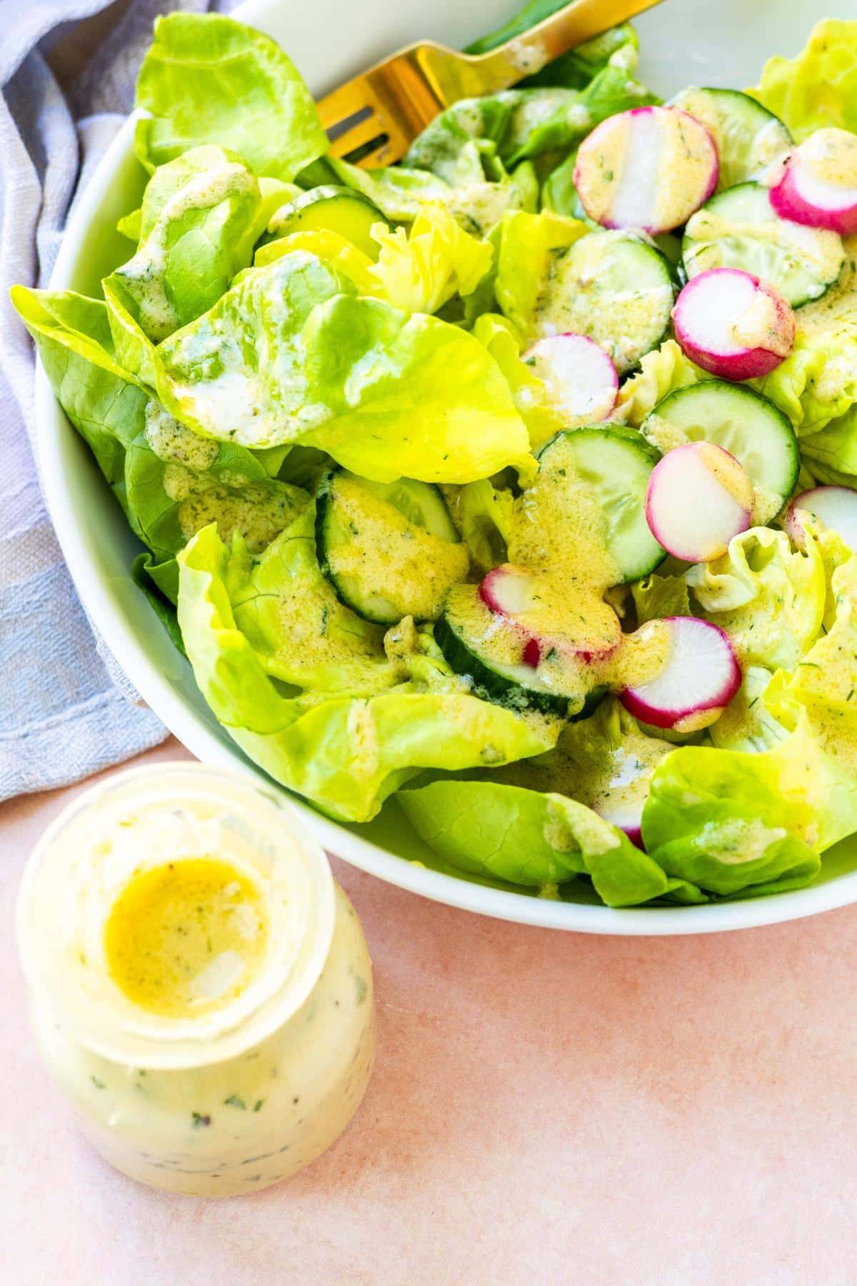 A bottle of hummus dressing and a salad with the dressing drizzled on top.