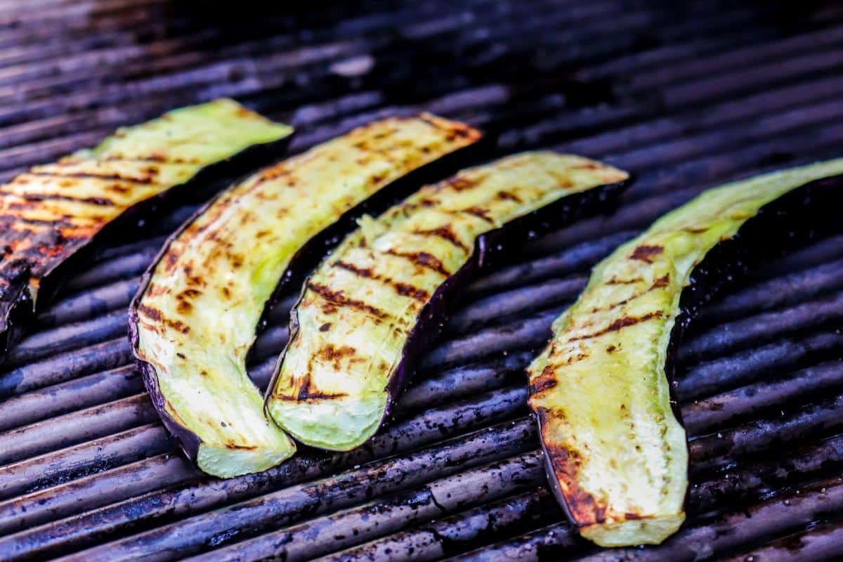 Eggplants sliced lengthwise cooking on a grill.