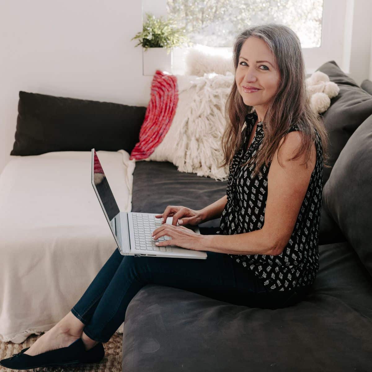 Amy from Veggies Save The Day sitting on a couch with her laptop.